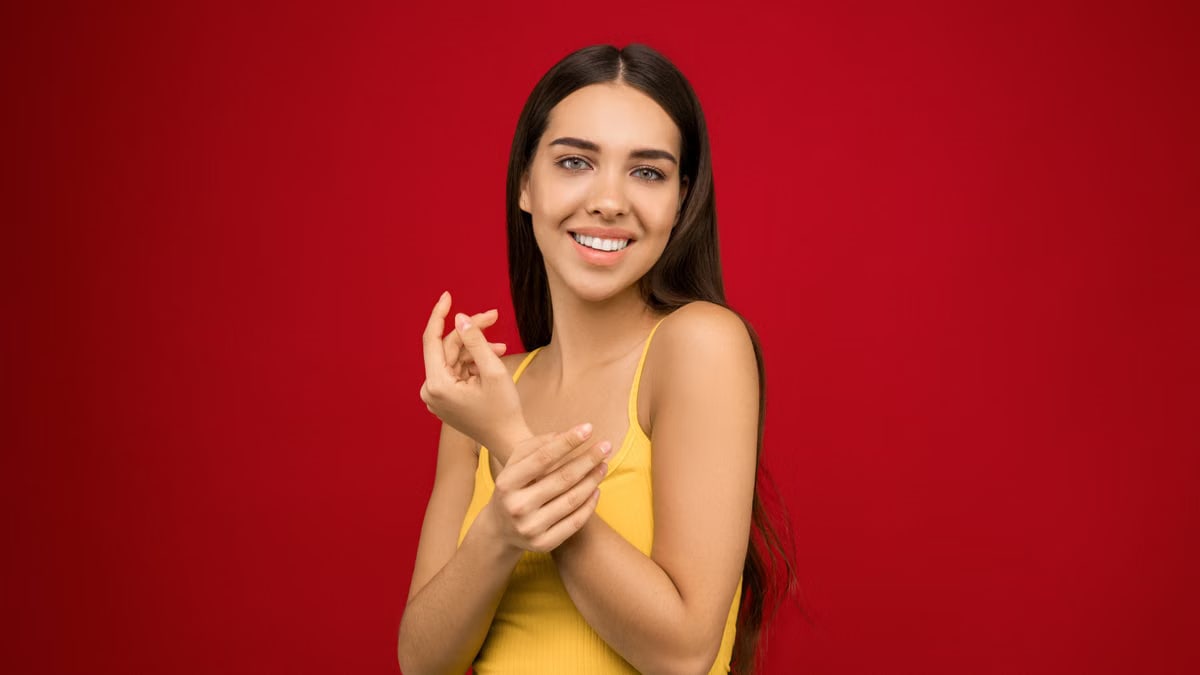 A cheerful woman poses in a yellow tank top against a vibrant red background.